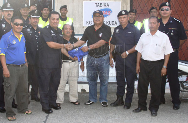 Adzhar (third left) hands over a goody bag to a village chief at Bukit Kuda community hall. Looking on are Douglas (third right), Sammy (right) and the rest of the police team members and village chiefs.