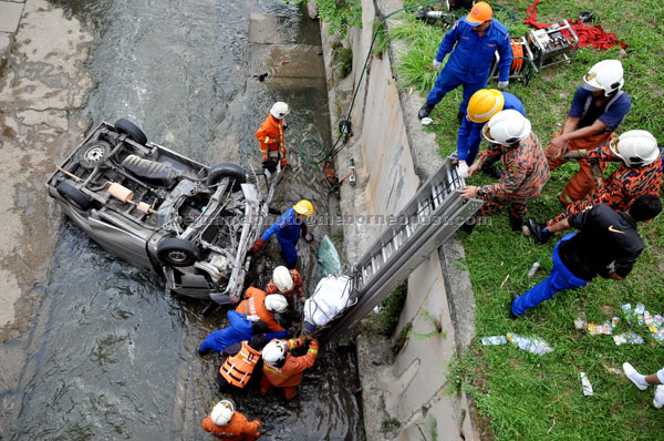 FATAL CRASH: Firemen bringing out the bodies from the crash site. — Bernama photo