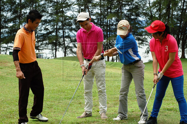 CAREER IN GOLF INDUSTRY: File pix of Johari (extreme left), a caddy from Damai Golf and Country Club looking at club executive Lily Stephens (centre) giving tips to young golfers.