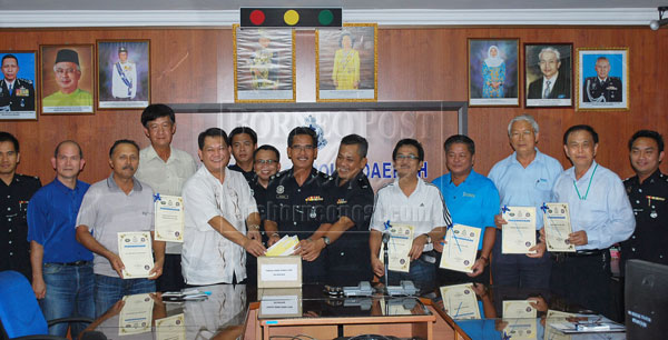 NOBLE DEED: Madang (centre), Mohd Said (sixth right) and others symbolically putting the cheques into the box during the donation presentation ceremony at Bintulu police headquarters yesterday. 