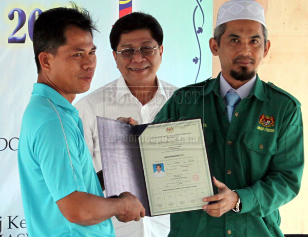 SAFETY FIRST: Hatta (right) presenting a certificate of competency to a worker at the site of the Unimas student hostel. 