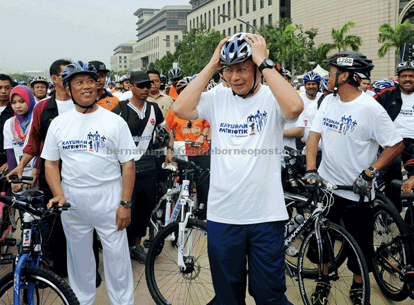 GETTING READY: Najib adjusts his helmet during 1 Malaysia Patriotic Cycling event in Putrajaya while Deputy Prime Minister Tan Sri Muhyiddin Yassin (left) looks on. — Bernama photo  
