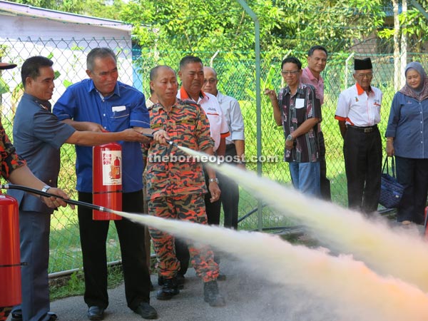 Len (second left) assisted by Suna trying out a fire extinguisher during a demonstration. 