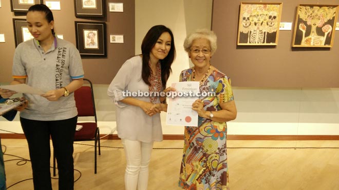 Wong (right) accepting her certificate from Jennifer during the launch of the 8th Sabah Women Art Exhibition at the Sabah Art Gallery.