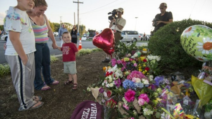 © AFP / by Glenn Chapman | A family pays their respects at a makeshift memorial for reporter Alison Parker, and cameraman Adam Ward at the gate of WDBJ television studios August 26, 2015, in Roanoke, Virginia