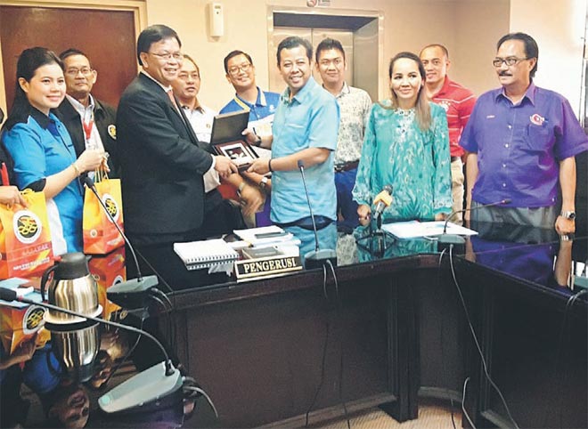 Affandi and Razlan (fifth right) in jovial mood while exchanging souvenirs at the end of the Sukma briefing in Kuching yesterday.