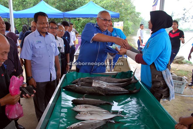 Zaiedy distributing an apron to one of the traders at the market as Azrin (left) looks on.