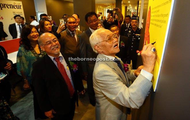 Taib (right) signs a commemorative poster on the wall of the ICube office as Liew (left) and others look on.