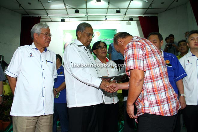 Manyin (left) looks on as Adenan presents a land title to one of the recipients. — Photo by Chimon Upon 