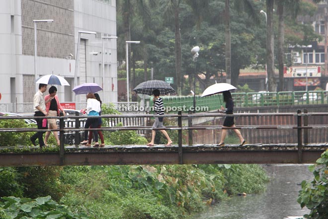 Pedestrians shielding themselves from the rain while crossing a bridge at Pending yesterday. — Photo by Chimon Upon