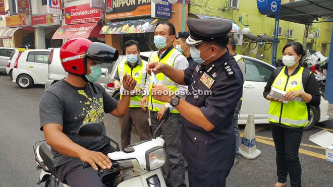 Kuching police chief ACP Roslan Bek Ahmad helps put a facemask on a motorcyclist in front of the Padungan police station. At Roslan’s right is Community Policing Sarawak head Datuk John Lau.