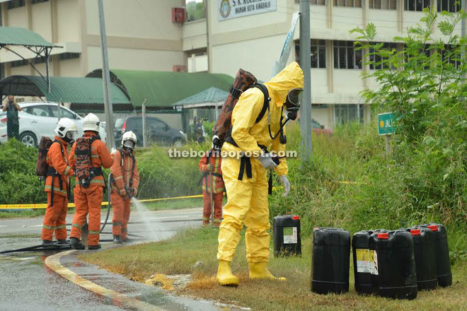 A Fire and Rescue Services personnel from the Hazmat Unit inspecting the barrels that fell off the lorry near SK Kelombong in Inanam yesterday.