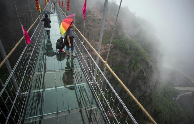 Chinese tourists walk across a glass-bottomed suspension bridge in the Shinuizhai mountains in Pingjang county, Hunan province some 150 kilometres from Changsha. — AFP photo