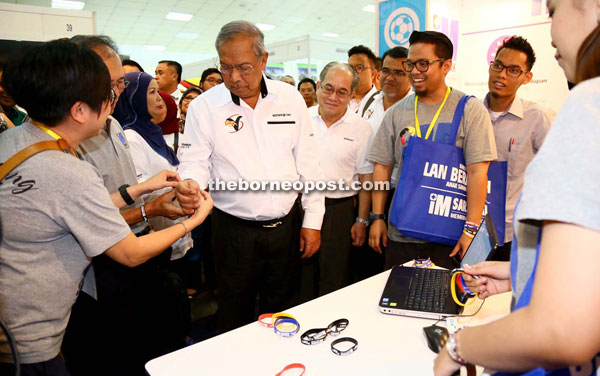 Adenan tries on a ‘hand band’ during his visit to a booth at an exhibition held as part of the Lan Berambeh Anak Sarawak 2015 programme.
