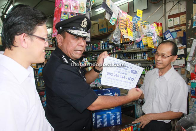 Roslan presents the 24-hour Kuching police hotline number to a business owner.   At left is Sih. — Photo by Jeffery Mostapa