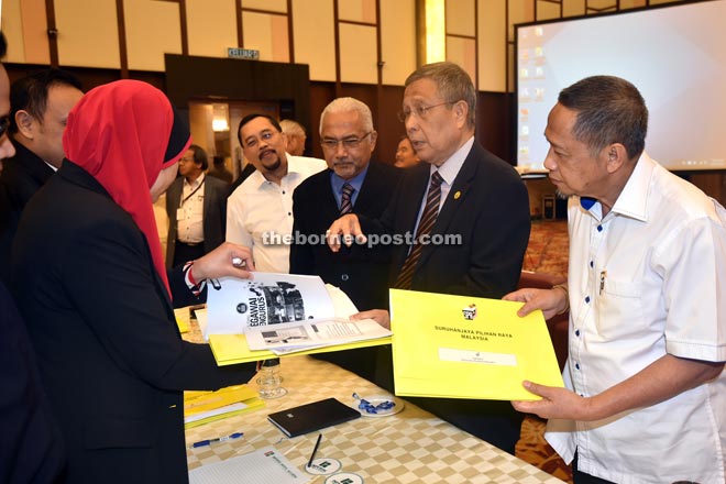 Abdul Aziz (second right) presents a file containing guidelines to a participant of the briefing and training session yesterday. Takun is at right. — Photo by Chimon Upon