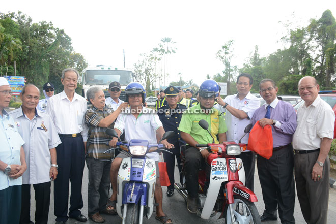 Dr Abdul Rahman (third right) and Paulus (fourth left) in the presence of others including Maria (second right) assisting motorists to put on safety helmets during the road safety campaign.