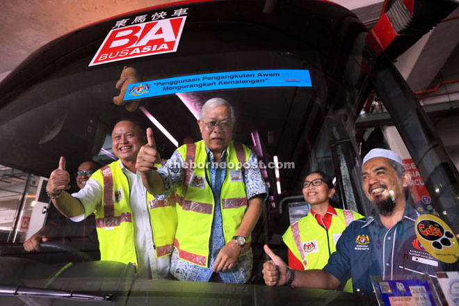 Manyin (third left) together with (from second left) Chan, Davina and Mohd Hatta giving their thumbs-up after Manyin fixes the road safety message sticker on a bus yesterday.