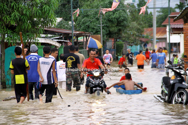 A man riding his motorcycle through the flood at Kampung Bintawa Tengah — Photo by Chimon Upon