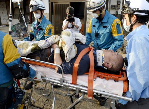 A man is carried away by a rescue workers after being rescued from his collapsed home caused by an earthquake in Mashiki town, Kumamoto prefecture, southern Japan, in this photo taken by Kyodo April 16, 2016. Mandatory credit REUTERS/Kyodo