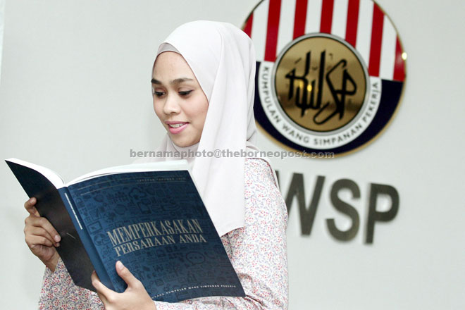 An EPF employee takes a look at the EPF’s 2015 Annual Report after its unveiling. — Bernama photo