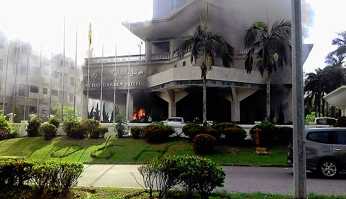 Thick black smoke billows from the lobby area of Orchid Garden Hotel when a Mercedes-Benz suddenly catches fire while in a parked position. | PHOTO: WHATSAPP, brudirect.com