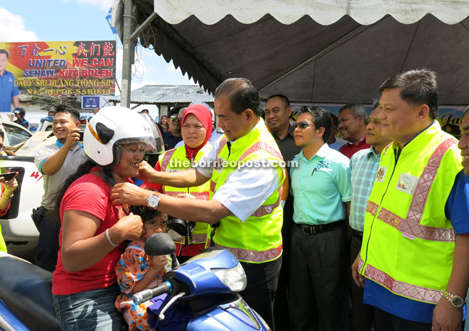 Aziz puts on a new helmet on to a motorcyclist, as Huang (right) and others look on.