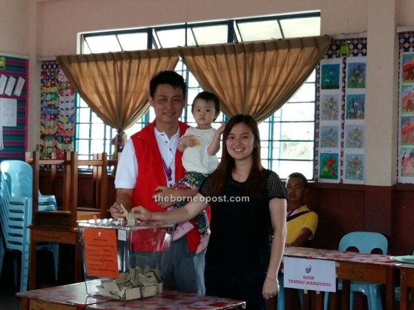 DAP candidate for Piasau, Alan Ling Sie Kiong carrying his 24-month-old daughter, as he casts his vote with his wife, Florence Lau Bern Ee, at SK St Joseph, Miri at 9 am.