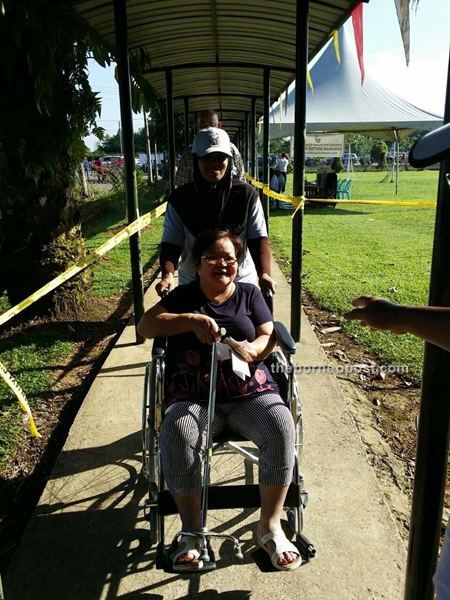 A woman in wheelchair is wheeled to the polling station by an Election Commission worker at SK Garland.