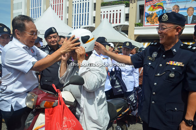 Wong (left) helps a motorcyclist to put on the safety helmet as Mazlan (second left) and Koo (right) look on.