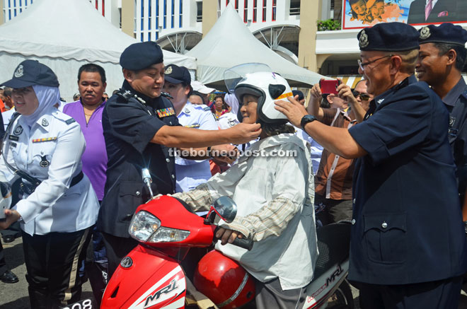 Mazlan (third left) helps a motorcyclist to buckle up her helmet as Koo (right) looks on. 