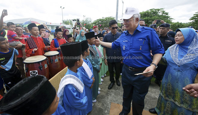 Najib greets some of the SK Pusa students welcoming him to the school opening event. At right is school headmistress Hamisah Ahmad. — Bernama photo