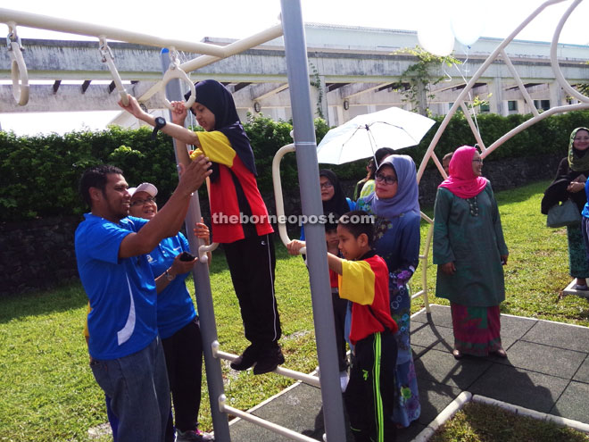 NEW CHALLENGE: Minister of Welfare, Women and Community Wellbeing Datuk Fatimah Abdullah looks on closely as a child attempts a hanging routine at a children’s playground at the State Library yesterday. She calls on libraries across the state to set up basic play facilities for kids. 