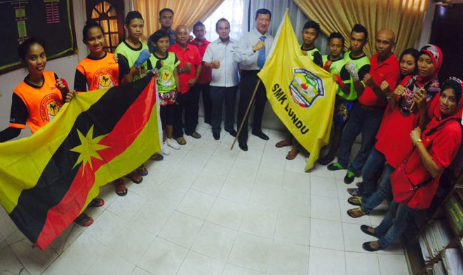 SMK Lundu principal Nazamuddin Alias presents the state flag to Lim Min Chiong while the representative of Lundu District senior administrative officer Kenny Paul and others look on.