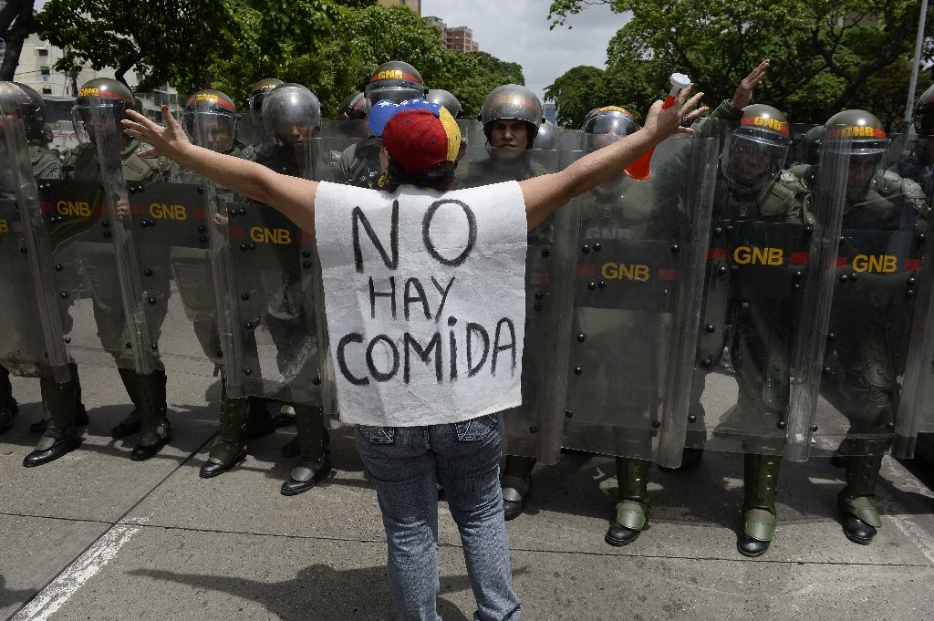 A woman with a sign reading "There is no food" protests against new emergency powers decreed by President Nicolas Maduro in front of police in Caracas. Photo by AFP