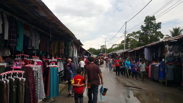 Shoppers walk along the tar-sealed street, flanked by a long line of stalls.