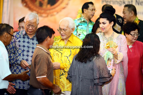 Taib, flanked by Raghad and Manyin, presents aid to recipients.