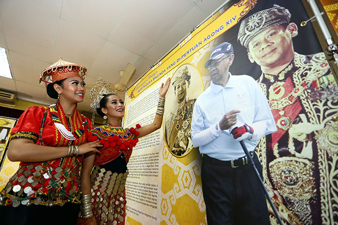 OUR RULER: Cultural performers Nursharmilya Amira Anuar (left) and Hartinah Abdullah take a closer look at a panel that displays photos and background of the reigning Yang di-Pertuan Agong Tuanku Abdul Halim Mu’adzam Shah at the special ‘Raja Kita’ exhibition in Serian Community Hall yesterday. — Photo by Muhamad Rais Sanusi