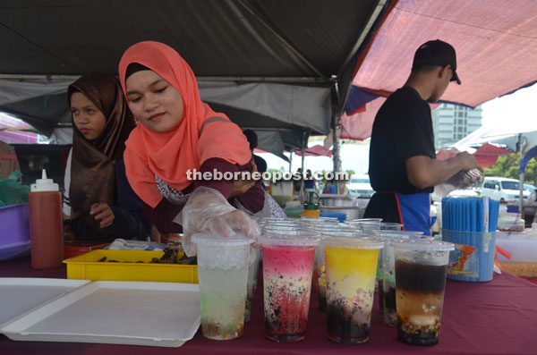 Vendors arrange colourful drinks at their stall, ready to be grabbed by customers. 