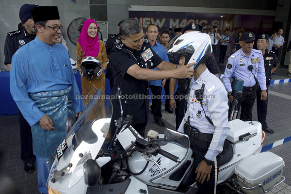 Khalid (centre) putting on a safety helmet on a police traffic officer at the handing out of crash helmets to traffic policemen programme in Menara Celcom. Shazalli is at left. — Bernama photo