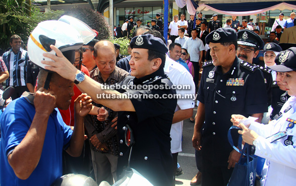 UNTUK KESELAMATAN: Mazlan memakaikan topi keledar lebih selamat kepada penunggang motosikal pada pelancaran Ops Selamat sempena Aidilfitri di Kota Samarahan, semalam.