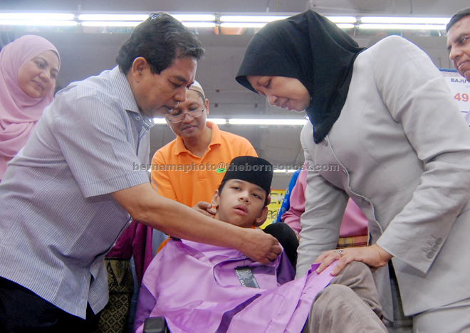 Dr Hilmi and wife Datin Hajjah Jamilah Mohd help a special needs child Muhd nur Artifin Nazeel Norjis, 16, try on a set of Baju Melayu for the coming Hari Raya at the Mydin supermarket at Bukit Jambul. — Bernama photo