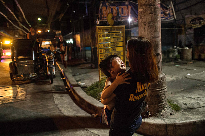 A social worker holds a child after a night-time curfew had passed in Manila. Armed police are detaining crying children, bewildered drunks and shirtless men throughout the Philippine capital in a night-time blitz that is offering an authoritarian taste of life under Duterte. — AFP photo