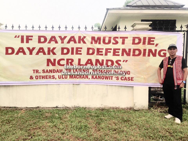 A photo of the late Bill posing in front of a banner hung up at the fence of the courthouse in Kuching last year when an NCR case involving TR Sandah, TR Lajang, Semawi Paong and few others was being heard in court. — Photo taken from Bill Kayong’s Facebook page.