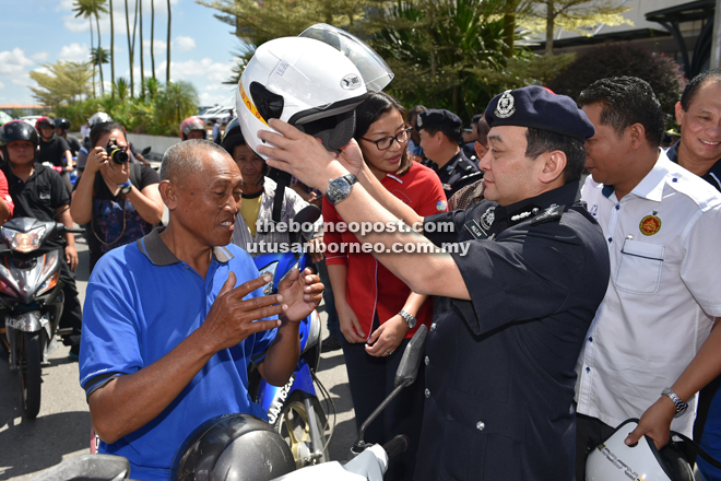 Mazlan presenting a new helmet to a motorcyclist during Op Selamat 9 in Kota Samarahan yesterday.