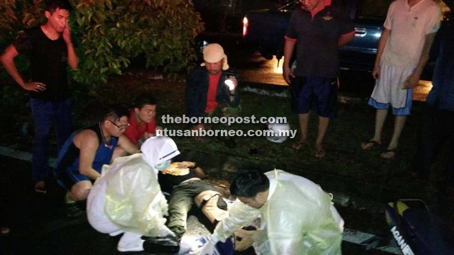 Paramedics from Miri Hospital checking the victim upon arrival at the scene while other concerned motorists look on.