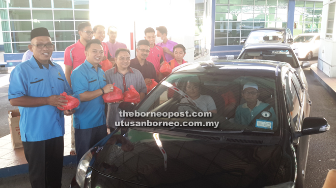 Roy (second from left) hands over `iftar’ to a motorist crossing the Sungai Tujuh Immigration Checkpoint yesterday. With him are Immigration Department personnel and Teacher Training Institute trainees. 