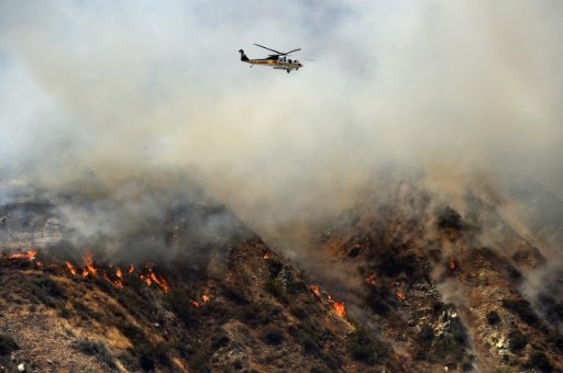 A water-dropping helicopter flies over burning hills in Azusa, California on June 20, 2016. Photo by AFP