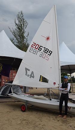 A windsurfer stands beside her equipment.