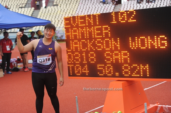 Wong has his picture taken with the scoreboard which depicts his gold winning feat of 50.82m.
